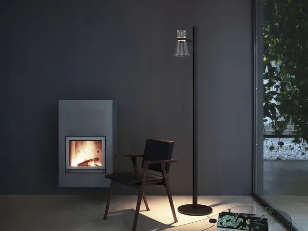 A residential interior at dusk lit by a single floor lamp and a fire